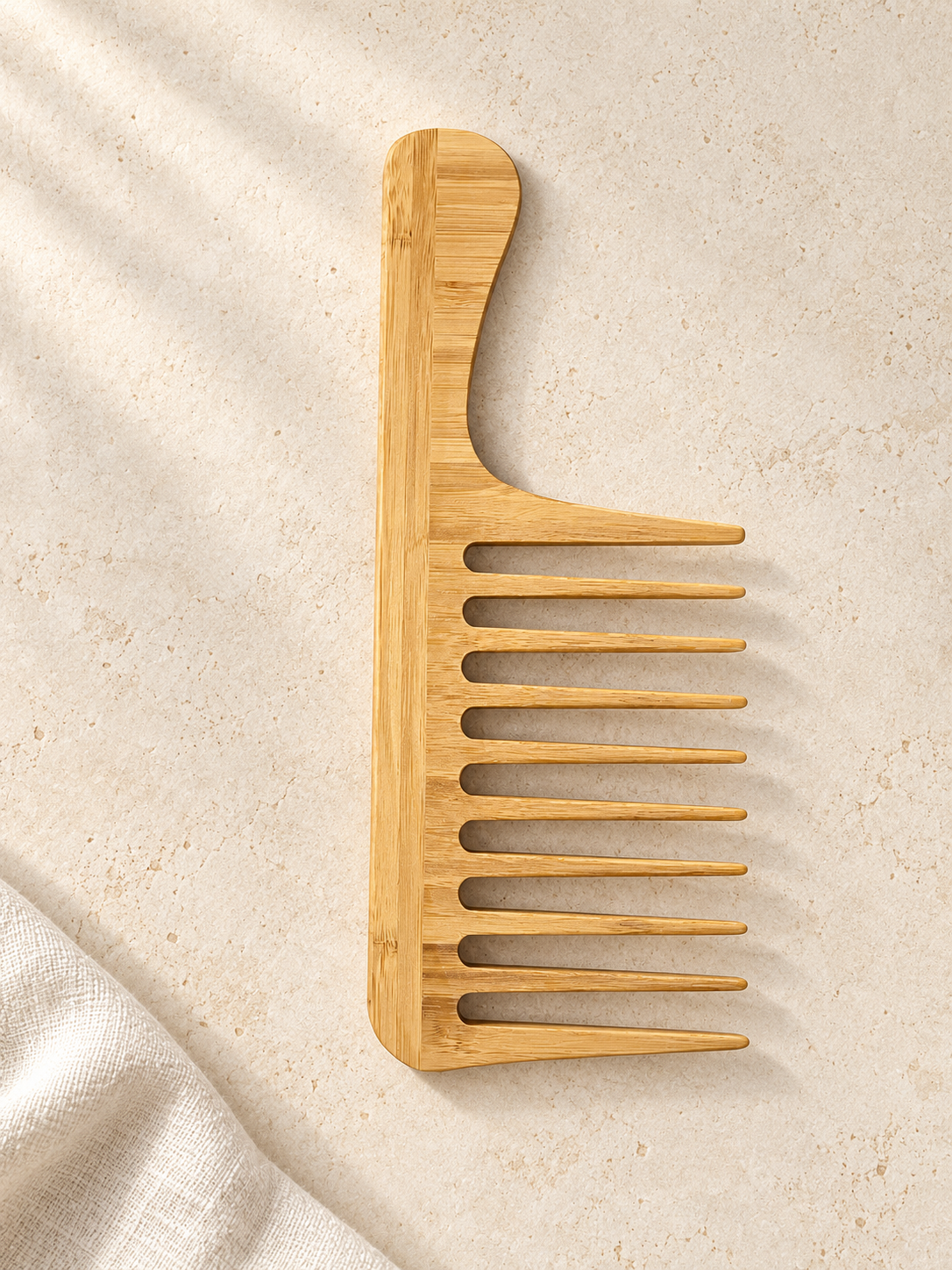 The full bamboo comb with ten widely spaced teeth and a long curved handle, on a warm ivory studio background.